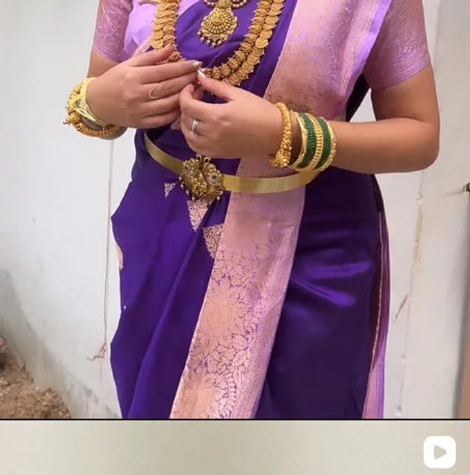 A purple silk saree worn with a gold vaddanam waist belt and bangles